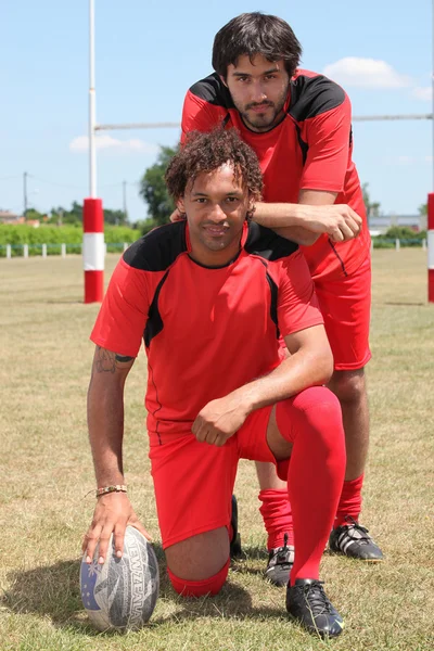 Två rugbyspelare poserar med bollen framför mål — Stockfoto
