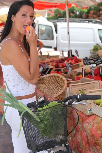 Summery woman eating an apricot at a market stall — Stock Photo, Image