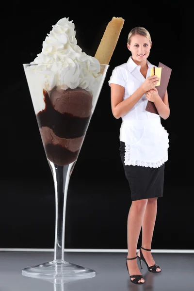 Красивая блондинка-официантка, стоящая на столе возле гигантского мороженого — стоковое фото