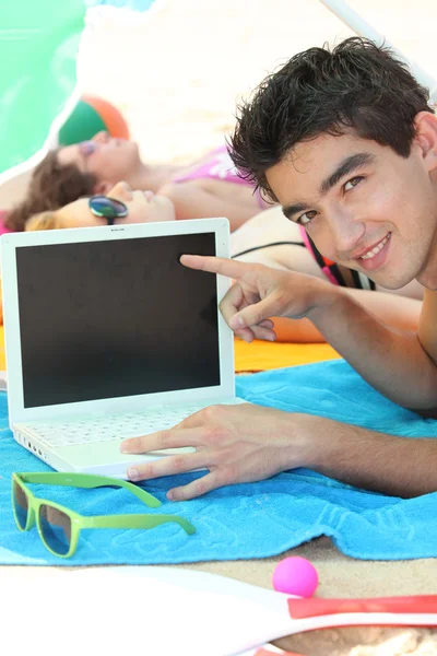 Un jeune homme sur la plage montrant un ordinateur — Photo