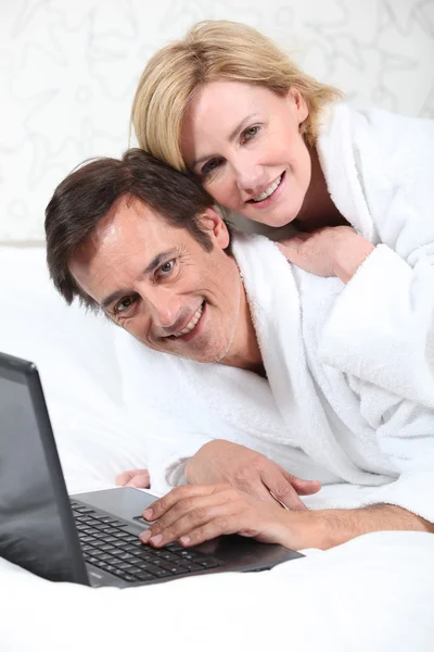 드레싱 가운에 휴대용 퍼스널 컴퓨터에 행복 한 커플. — 스톡 사진