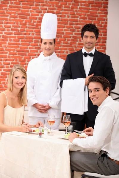 A couple being served by a waiter and a chef in a restaurant Stock Picture