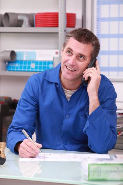 Man working in a plumber's merchants on the telephone clipart