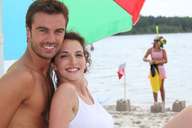 Couple on a sandy beach with daughter in the background clipart