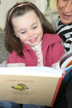 Young girl reading a book with the help of an adult clipart