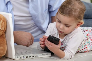 Young child playing with her father's mobile phone clipart