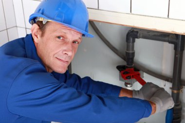 Plumber using a wrench on a water pipe clipart