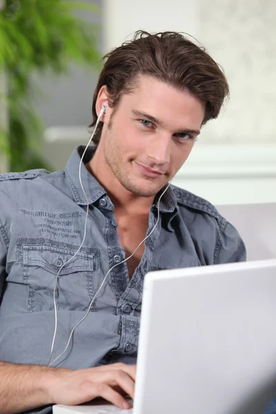 Jóképű férfi használja a fülhallgatót a laptop — Stock Fotó