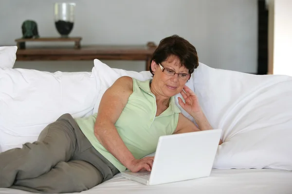 成熟的女人在沙发上使用她的笔记本电脑 — 图库照片