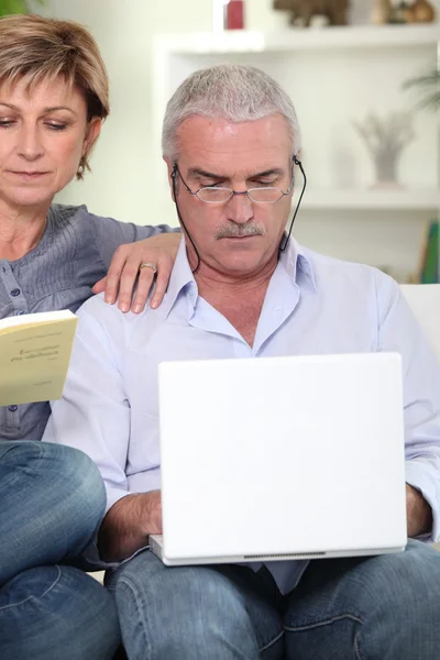 Casal de meia-idade sentou-se no sofá com laptop e livro — Fotografia de Stock