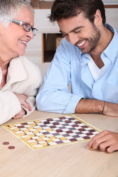 Молодой человек играет в шашки с женщиной постарше — стоковое фото
