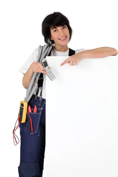 Eletricista com telefone mostrando painel branco — Fotografia de Stock