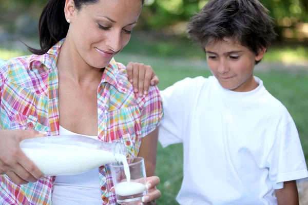 Mamãe derramando um copo de leite para seu filho — Fotografia de Stock