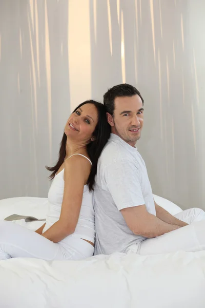 Par sitter rygg mot rygg på en säng — Stockfoto