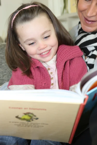 Νεαρή κοπέλα, διαβάζοντας ένα βιβλίο με τη βοήθεια ενός ενήλικα — Φωτογραφία Αρχείου