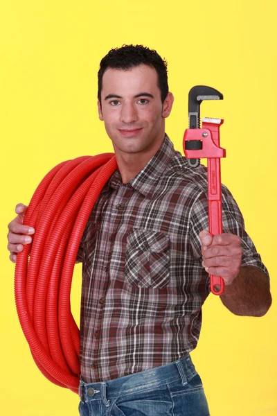 Craftsman holding a spanner and a pipe hose — Stock Photo, Image