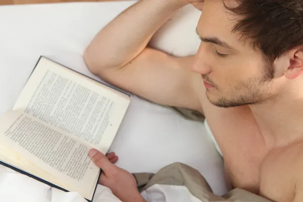 Молодой человек читает в постели — стоковое фото
