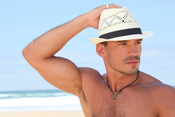 Muscular man posing on the beach in a panama hat — Stock Photo, Image