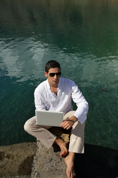 Hombre usando su portátil junto al borde del agua — Foto de Stock