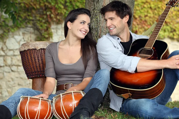 Couple playing drums and a guitar under a tree — Stock Photo, Image