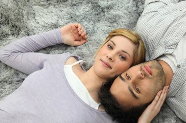Young couple lying top to tail on a grey carpet clipart