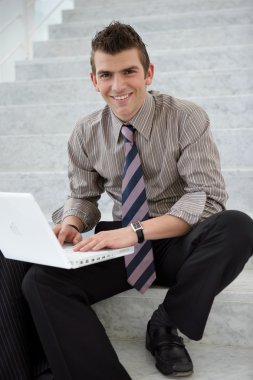 Young executive using a laptop computer on a stairwell clipart