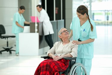 Hospital nurse pushing an elderly lady in a wheelchair clipart