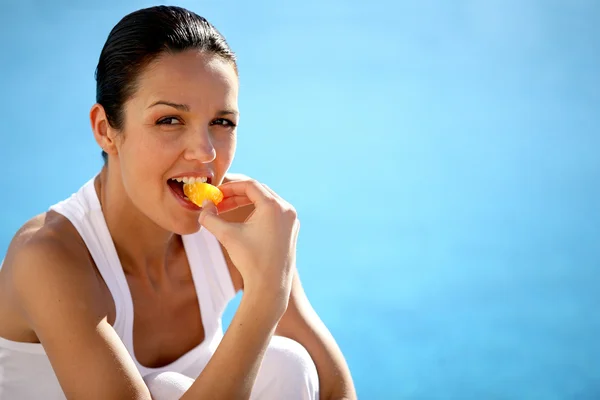 Mujer arrodillada junto a la piscina comiendo fruta — Foto de Stock