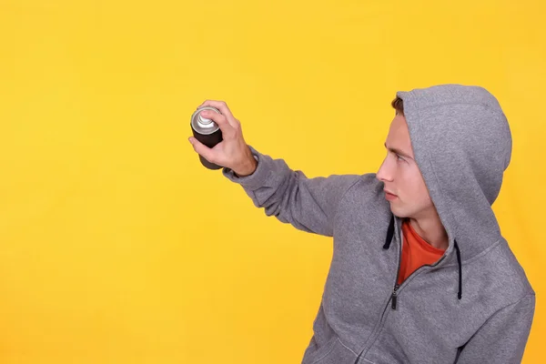 Teenager wearing hoodie against yellow background holding spray — Stock Photo, Image