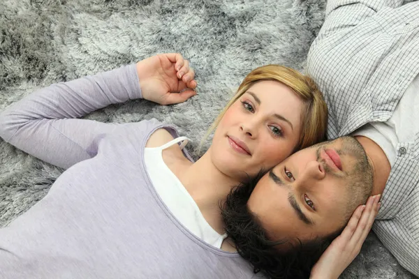 Mladý pár prolhaný shora k ocasu na šedý koberec — Stock fotografie