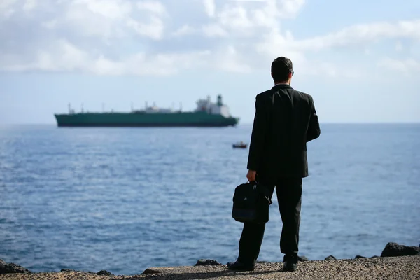 Businessman staring at a tanker out at sea — Stock Photo, Image