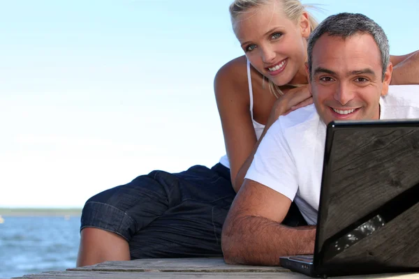 Ein Paar auf einem Ponton in der Nähe des Meeres, der Mann macht Computer, — Stockfoto