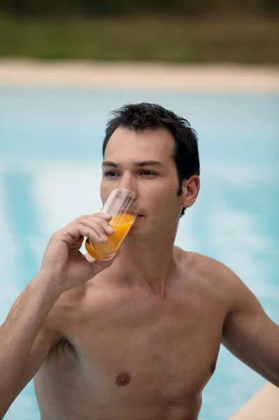 Muž pít pomerančový džus v bazénu — Stock fotografie