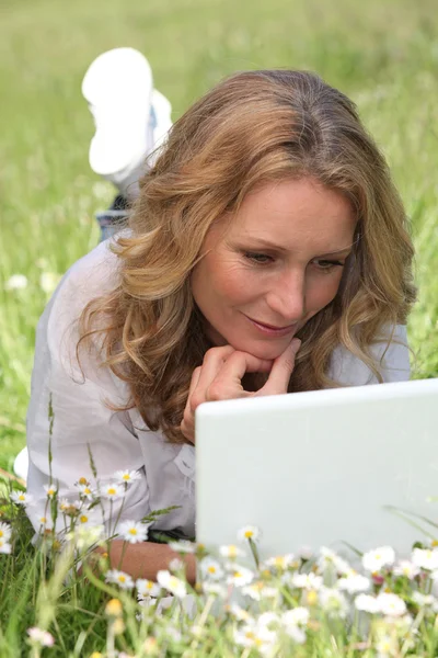 Entspannte Frau liegt mit ihrem Laptop in einem Margeritenfeld — Stockfoto