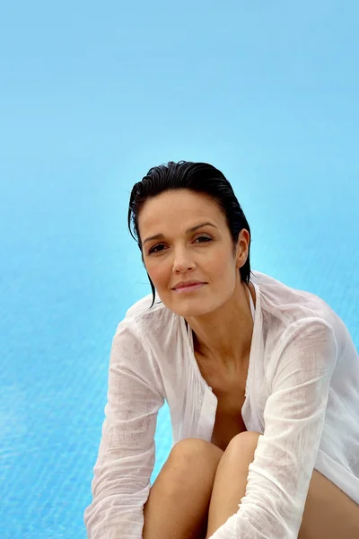 Morena vestindo camisa molhada sentada à beira da piscina — Fotografia de Stock