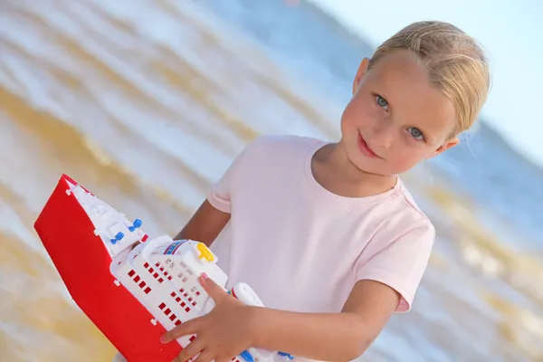 Menina loira brincando com um barco perto do mar — Fotografia de Stock