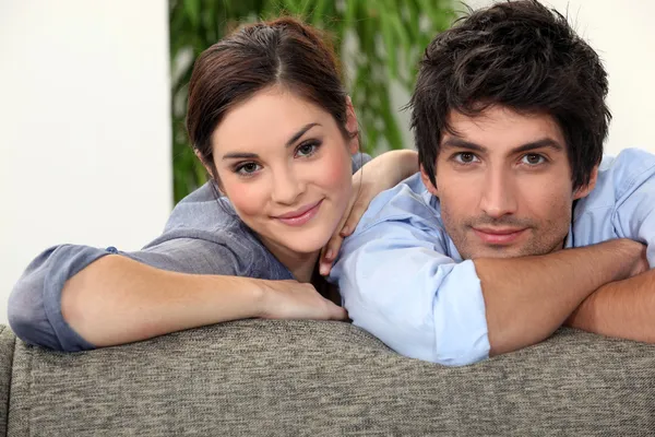 Hombre y mujer sonrientes apoyados en un sofá — Foto de Stock