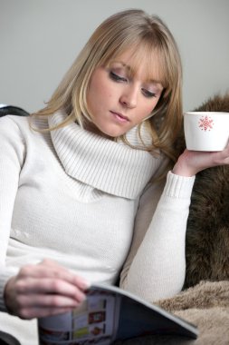 Attractive woman drinking a cup of tea and reading a magazine clipart