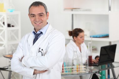 Smiling doctor cross-armed in lab clipart