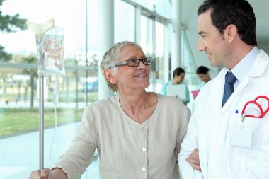 Doctor helping elderly patient in hall clipart