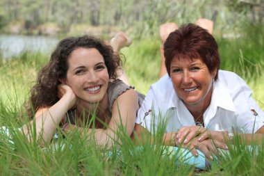 Older mother and adult daughter lying in the grass clipart