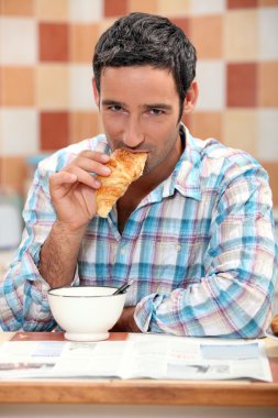 Handsome man eating a croissant clipart