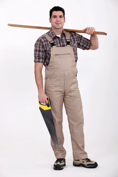 Carpenter carrying a plank of wood and a saw — Stock Photo, Image