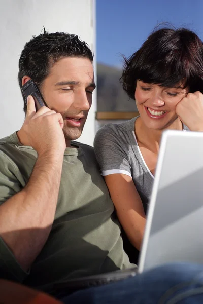 Pareja en el sol con un ordenador portátil y teléfono — Foto de Stock