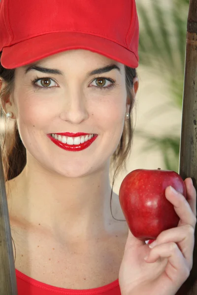 Молодая женщина в красной шапке с яблоком в руке — стоковое фото