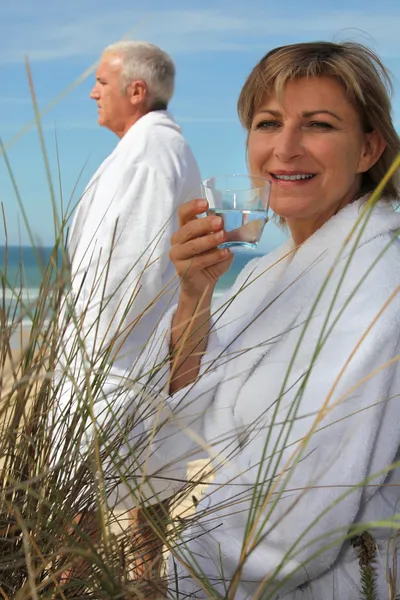 Een volwassen paar langs het strand in badjas. — Stockfoto