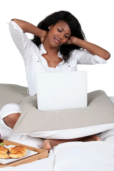 Чорна жінка схрещена ногами на ліжку з ноутбуком — стокове фото