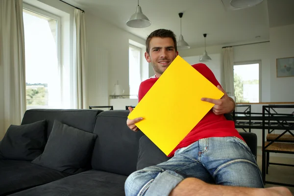 Мужчина сидит в своей гостиной и держит желтую вывеску — стоковое фото