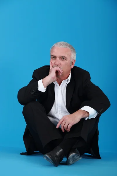Middle-aged man in black suit sitting on the floor — Stock Photo, Image
