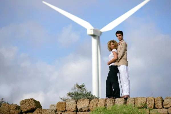 Casal em pé diante de uma turbina eólica — Fotografia de Stock